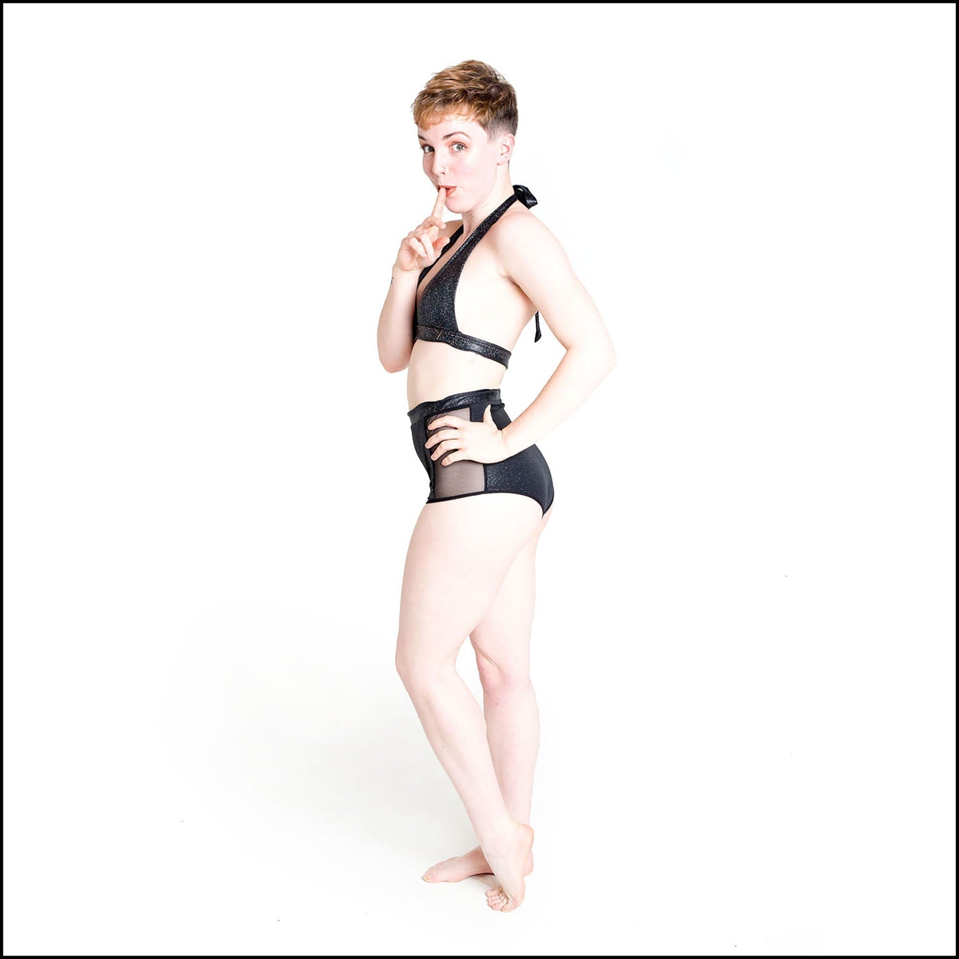 Cosmic Bikini in black hologram, foil printed spandex. The bikini features a tie halter neck top and high waist shorts bottoms with black mesh side panels. Side view. 