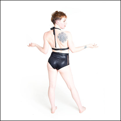 Cosmic Bikini in black hologram, foil printed spandex. The bikini features a tie halter neck top and high waist shorts bottoms with black mesh side panels. Back view.