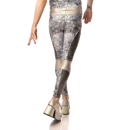 Disco Diva Leggings, a handmade-to-order piece in disco ball and silver foil print spandex. The leggings feature a double layer high waist with light silver knee panels and granite foil curved leg panels. Model Max stands with their back to the camera looking slightly over their shoulder. Image is cropped to show only the leggings.