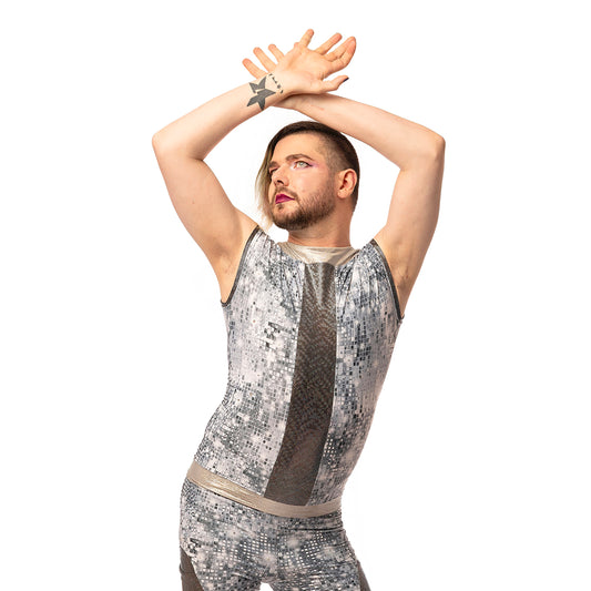 Disco Diva Leggings, a handmade-to-order piece in disco ball and silver foil print spandex. The leggings feature a double layer high waist with light silver knee panels and granite foil curved leg panels. Model Max stands with their hands crossed above their head. 