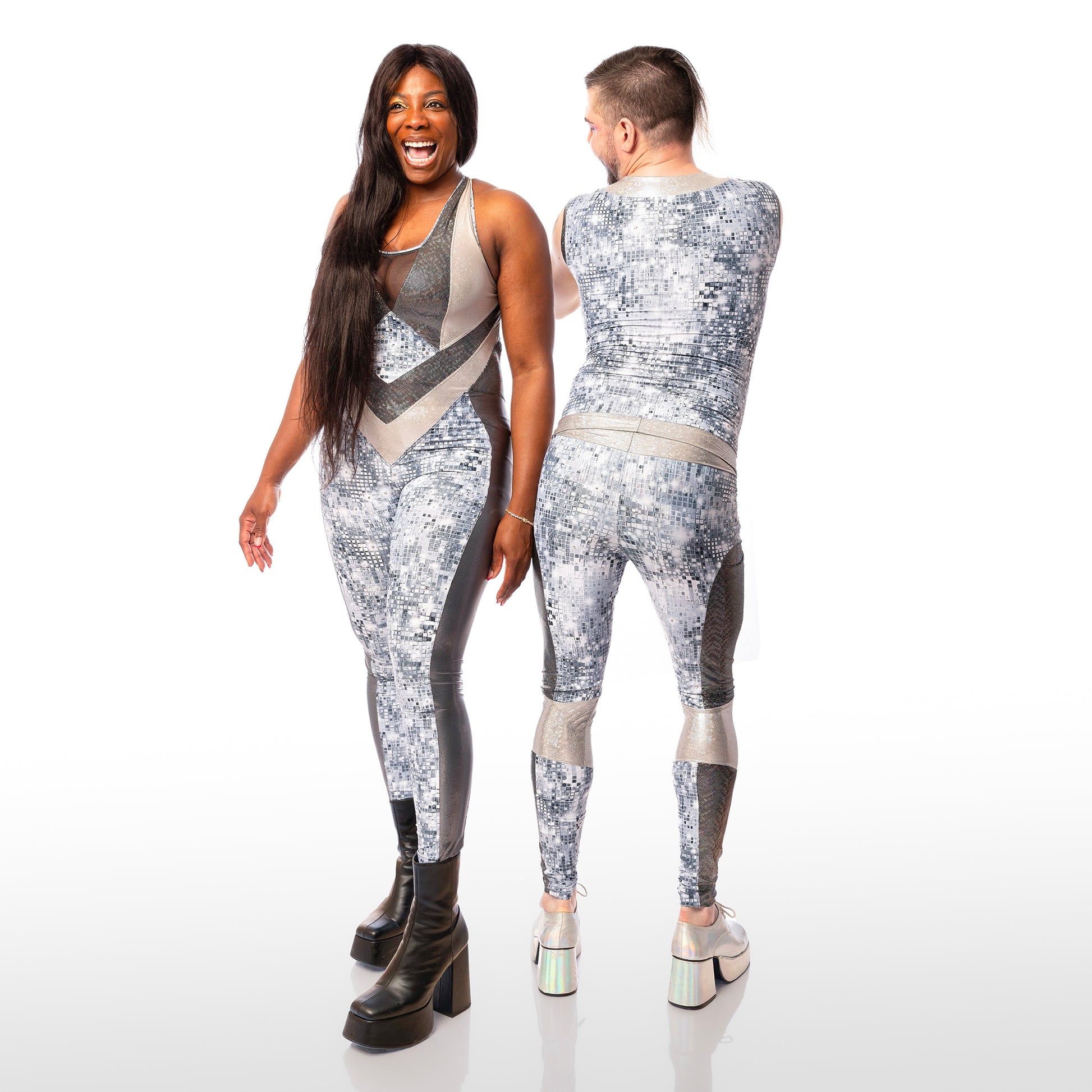 Disco Diva Leggings, a handmade-to-order piece in disco ball and silver foil print spandex. The leggings feature a double layer high waist with light silver knee panels and granite foil curved leg panels. Models Max and Roslyne stand side by side. Max has their back to the camera and Roslyne stands front on. Roslyne wears a matching catsuit. 