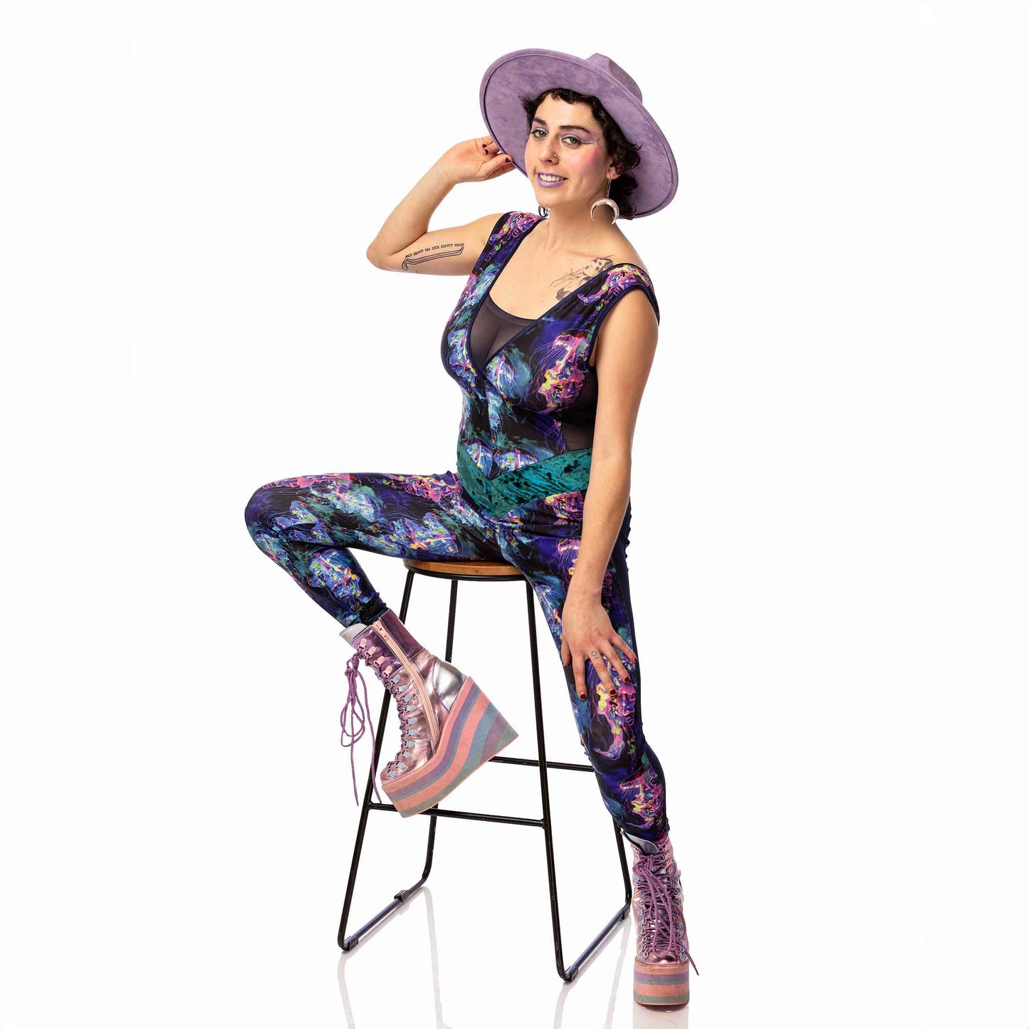 Jellyfish Catsuit, a handmade-to-order piece in purple, black, pink and green tropical jellyfish  printed spandex. This low back catsuit is both stylish and sustainable. The v-neck design features a flattering teal, foiled velvet waist panel and black mesh front insert and side panels.