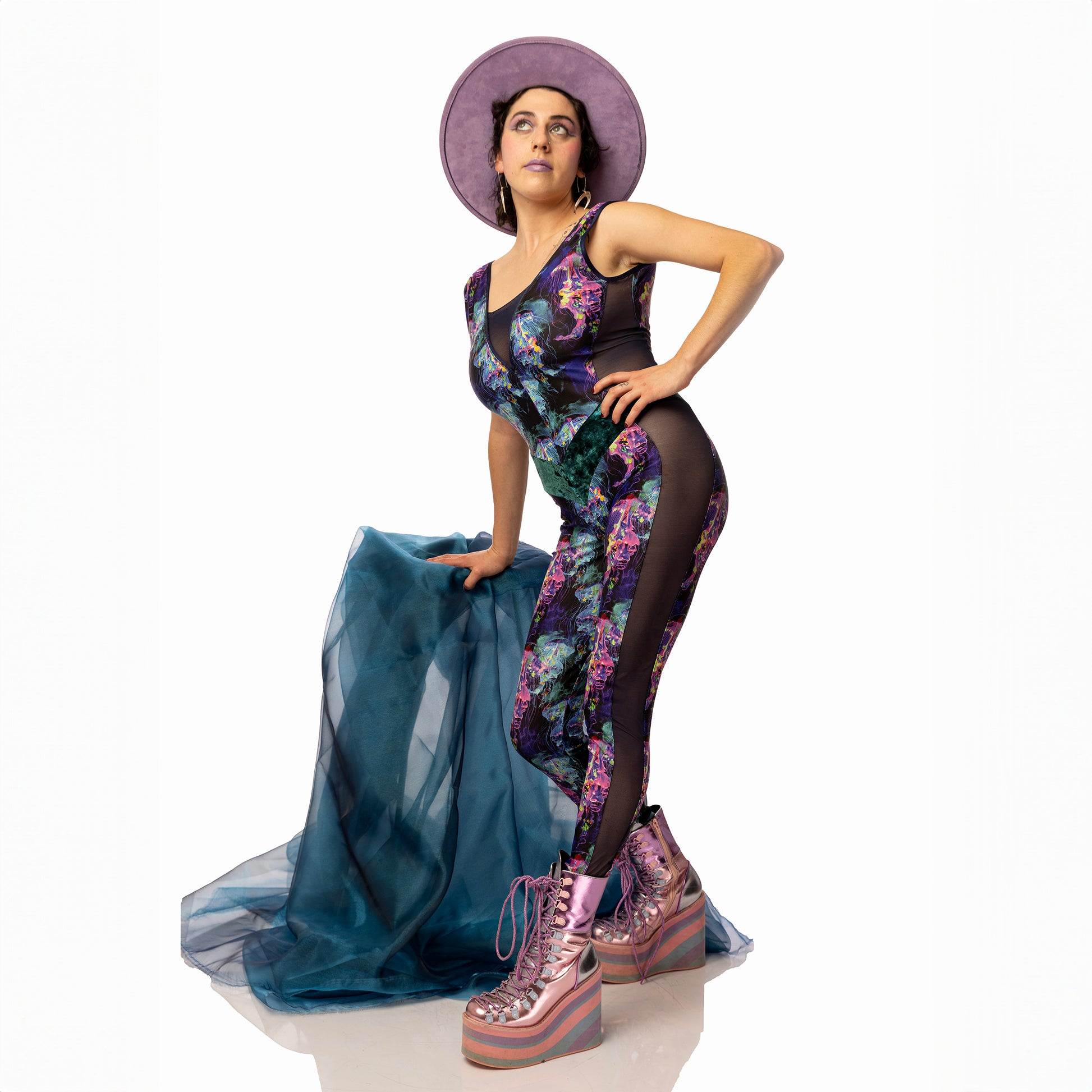 Jellyfish Catsuit, a handmade-to-order piece in purple, black, pink and green tropical jellyfish  printed spandex. This low back catsuit is both stylish and sustainable. The v-neck design features a flattering teal, foiled velvet waist panel and black mesh front insert and side panels.