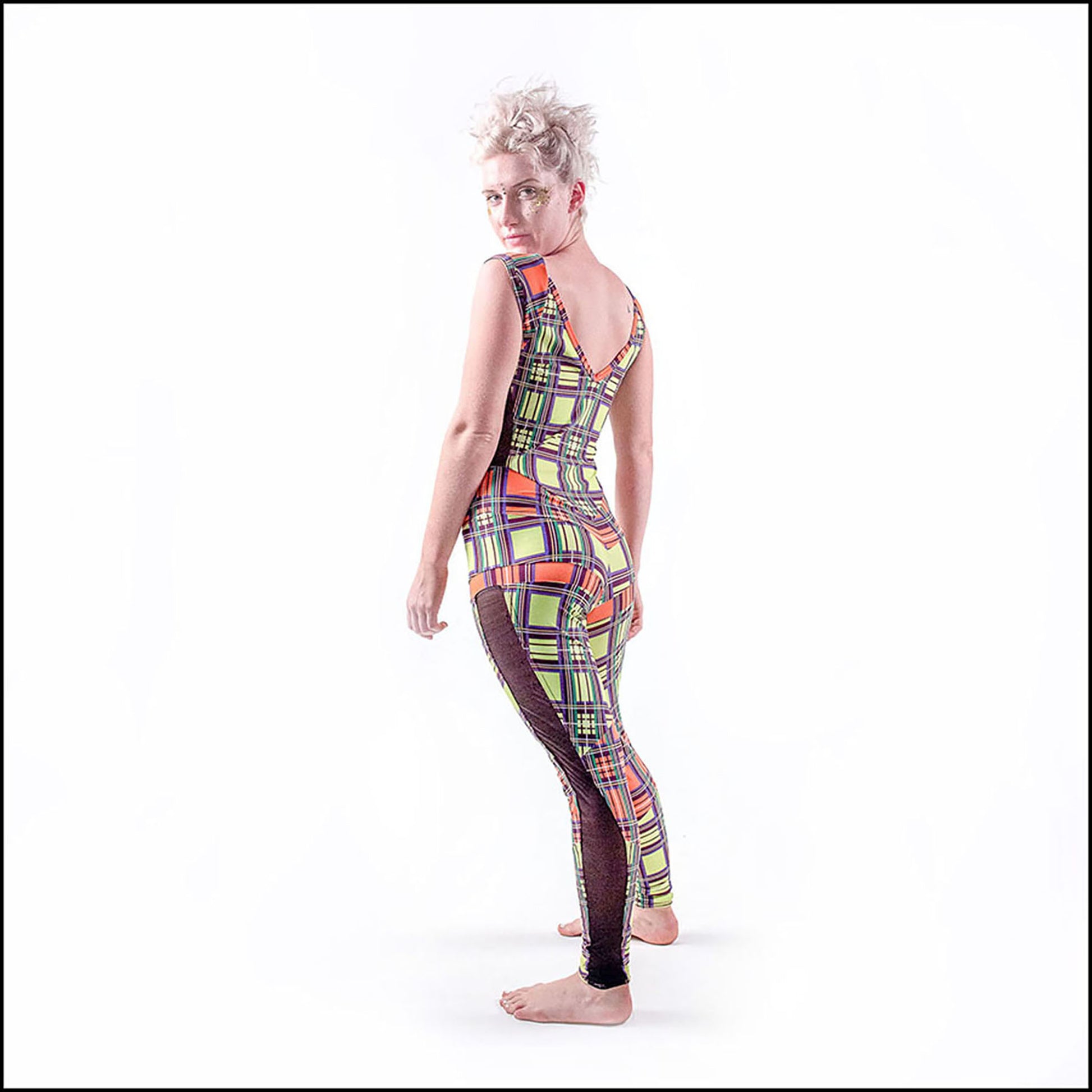 Neon Tartan Catsuit, a handmade-to-order piece in yellow and orange neon tartan printed spandex. This statement catsuit is both stylish and sustainable. The reversible design features a square mesh front neck and v-shaped back neck (for the style reversed see the Mardi Gras Catsuit). It includes black mesh side panels and multiple contrast panels. 