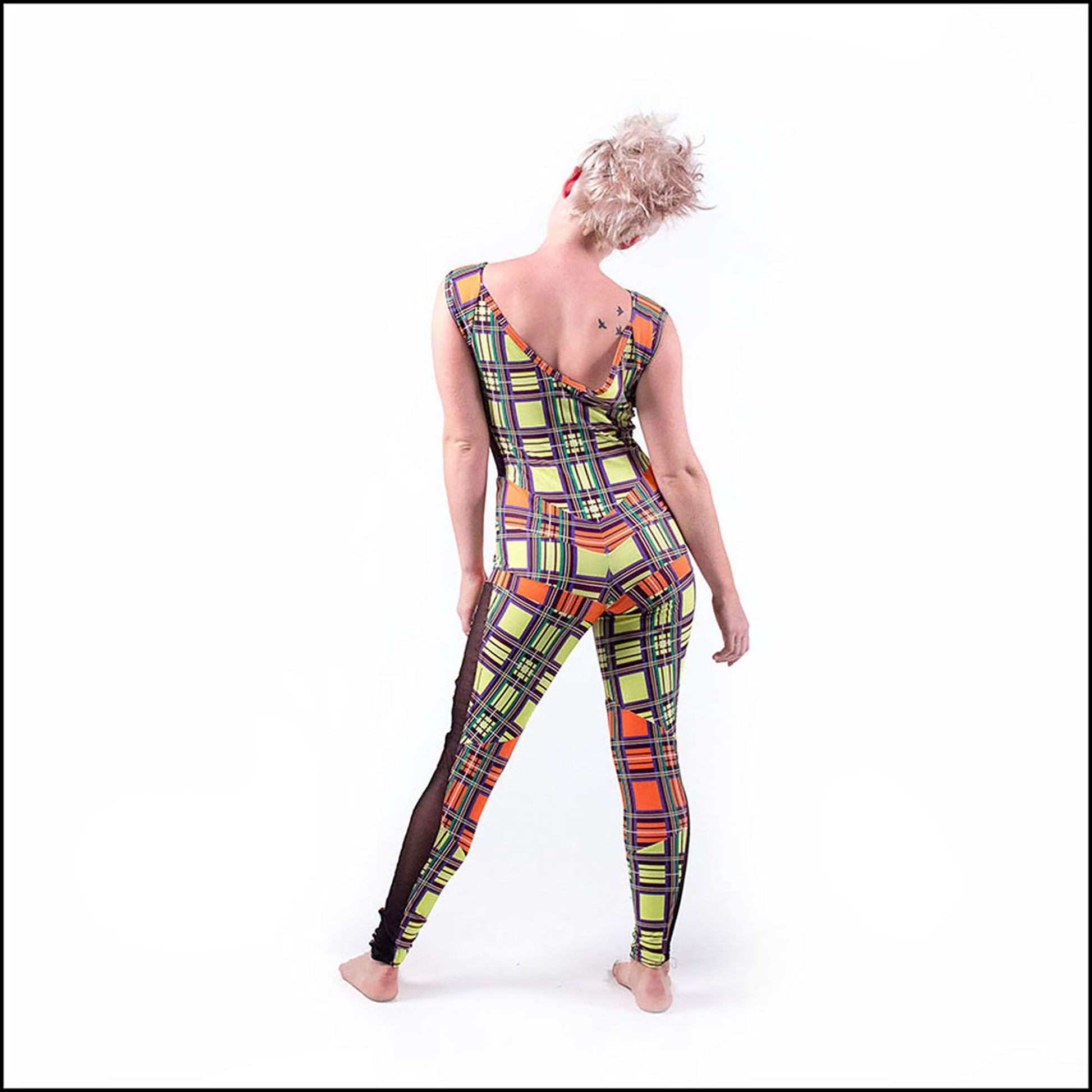 Neon Tartan Catsuit, a handmade-to-order piece in yellow and orange neon tartan printed spandex. This statement catsuit is both stylish and sustainable. The reversible design features a square mesh front neck and v-shaped back neck (for the style reversed see the Mardi Gras Catsuit). It includes black mesh side panels and multiple contrast panels. 