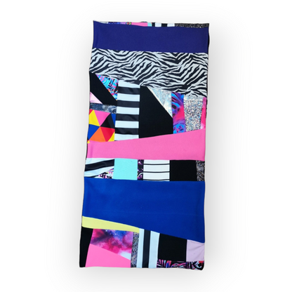 Large circular scarf made from recycled scrap fabrics.  Lined in black fleece and including bright, printed, multi coloured patchwork panels and large colour blocks in grey, pink, purple and blue. Pictured flat on white background. 