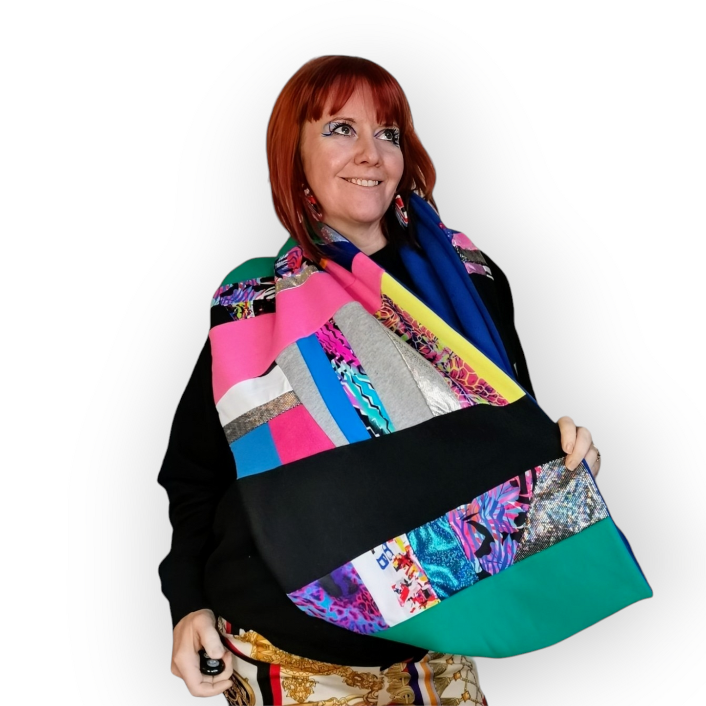Large circular scarf made from recycled scrap fabrics.  Lined in blue fleece and including bright, printed, multi coloured patchwork panels and large colour blocks in turquoise, pink, black and blue. Pictured on a model  hanging in a large loose circle around neck.  