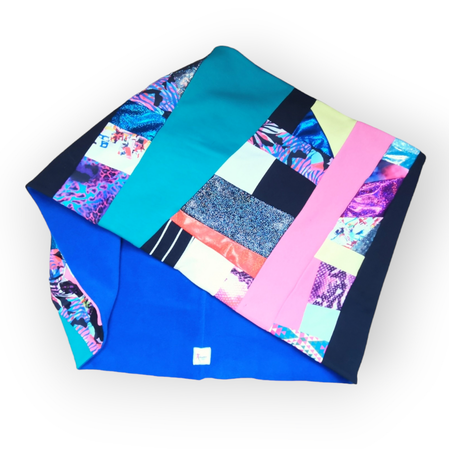 Large circular scarf made from recycled scrap fabrics.  Lined in blue fleece and including bright, printed, multi coloured patchwork panels and large colour blocks in turquoise, pink, black and blue. Pictured folded to show the outer and the lining on a white background. 