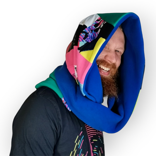 Large circular scarf made from recycled scrap fabrics.  Lined in blue fleece and including bright, printed, multi coloured patchwork panels and large colour blocks in turquoise, pink and yellow. Worn wrapped round twice and pulled over head like a hood.