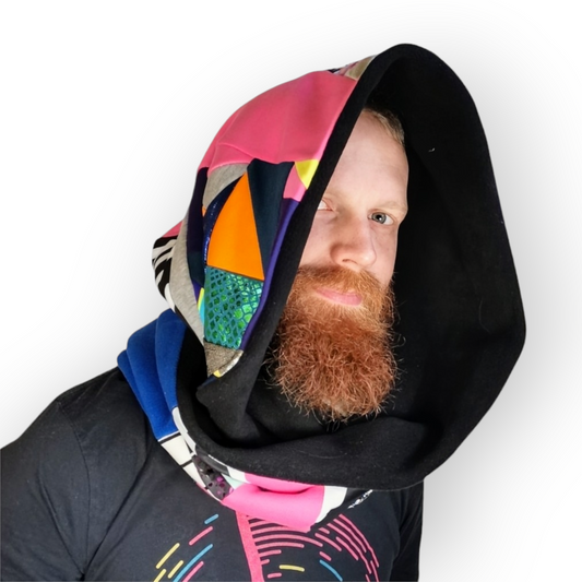 Large circular scarf made from recycled scrap fabrics.  Lined in black fleece and including bright, printed, multi coloured patchwork panels and large colour blocks in grey, pink, purple and blue. Pictured on model wrapped around neck and over head like a hood. . 