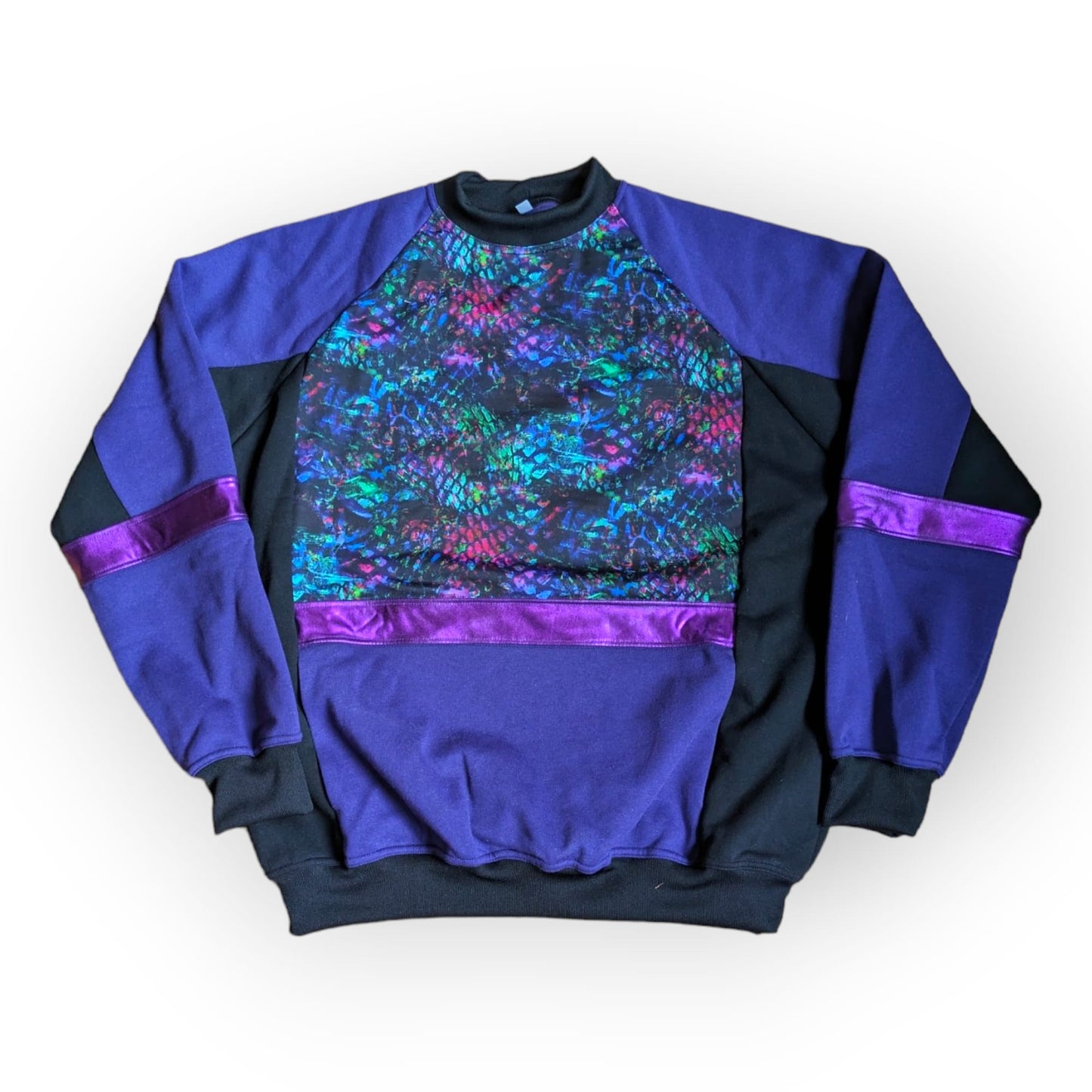 Flat front view of the Purple Snakebite Sweatshirt, a limited edition, off-the-peg piece in purple and black sweatshirt fleece with blue/green/pink snakebite print spandex details. The unisex design features a raglan sleeve, a large front pouch pocket, printed spandex chest panel and pink foiled stripes.
