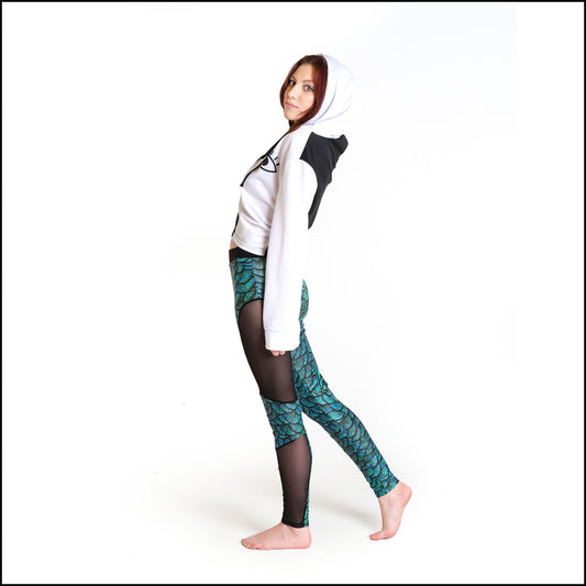 Draco Leggings, a handmade-to-order piece in aqua dragon scale printed spandex. These super cool leggings are both stylish and sustainable. The unisex design features a high double waistband, knee panels and black mesh side panels.