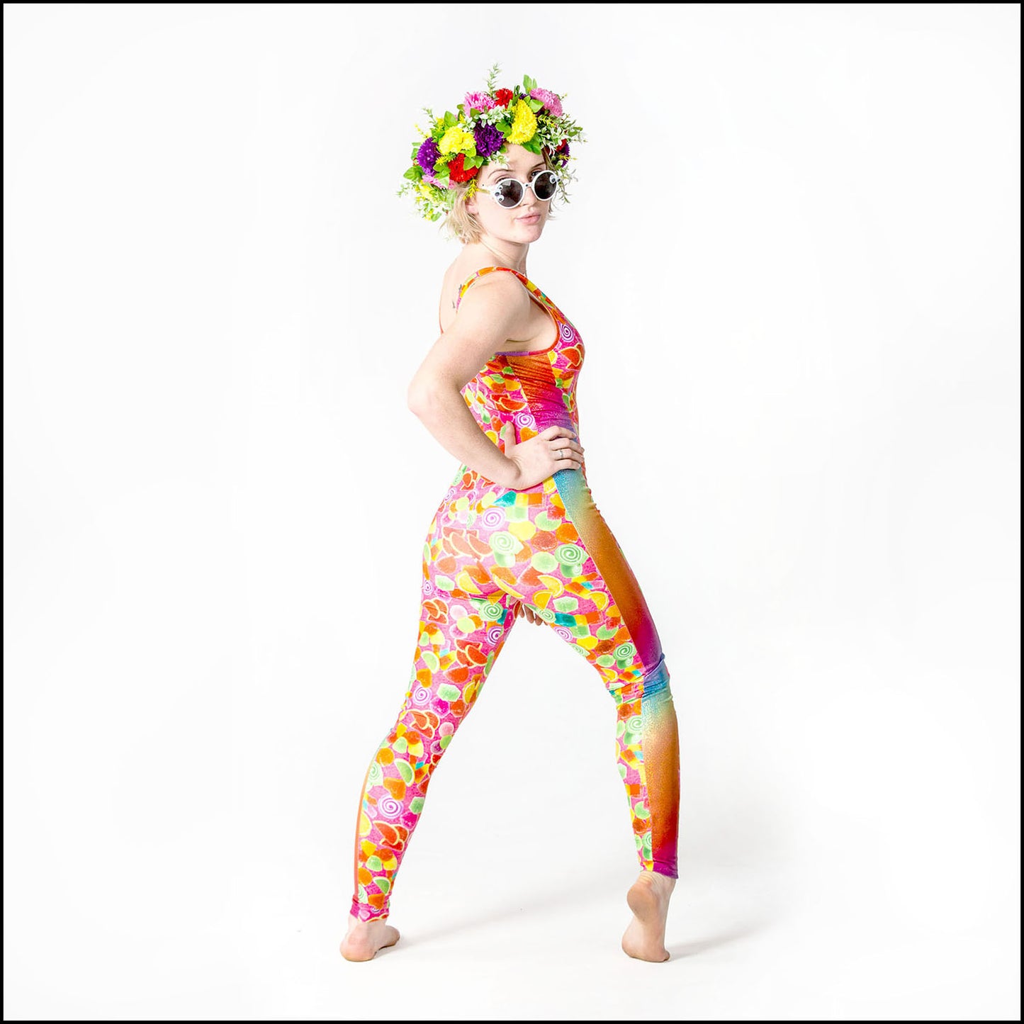 Pick 'N' Mix Catsuit, a handmade-to-order piece in pick 'n' mix candy printed spandex. This statement catsuit is both stylish and sustainable. The unisex design features a flattering V-neck with a rainbow hologram foil insert and full length side panels.