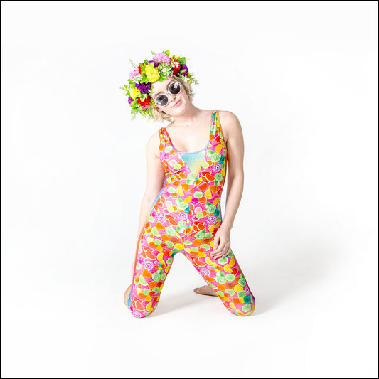 Pick 'N' Mix Catsuit, a handmade-to-order piece in pick 'n' mix candy printed spandex. This statement catsuit is both stylish and sustainable. The unisex design features a flattering V-neck with a rainbow hologram foil insert and full length side panels.