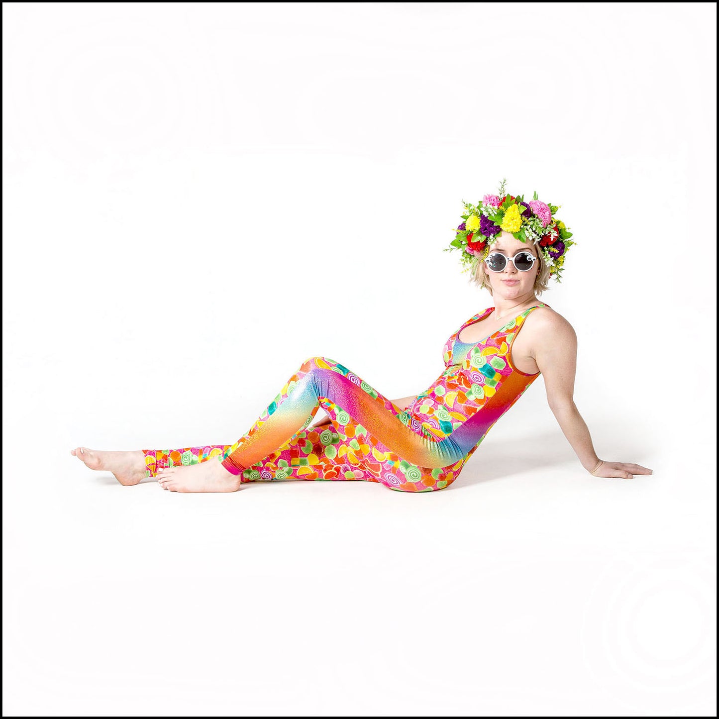 Pick 'N' Mix Catsuit, a handmade-to-order piece in pick 'n' mix candy printed spandex. This statement catsuit is both stylish and sustainable. The unisex design features a flattering V-neck with a rainbow hologram foil insert and full length side panels.